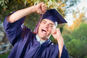 Happy Handsome Male Graduate in Cap and Gown Outside.