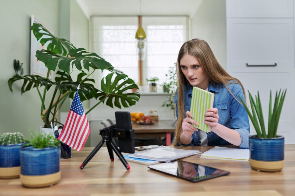 Young woman student studying at home online remotely, USA flag background